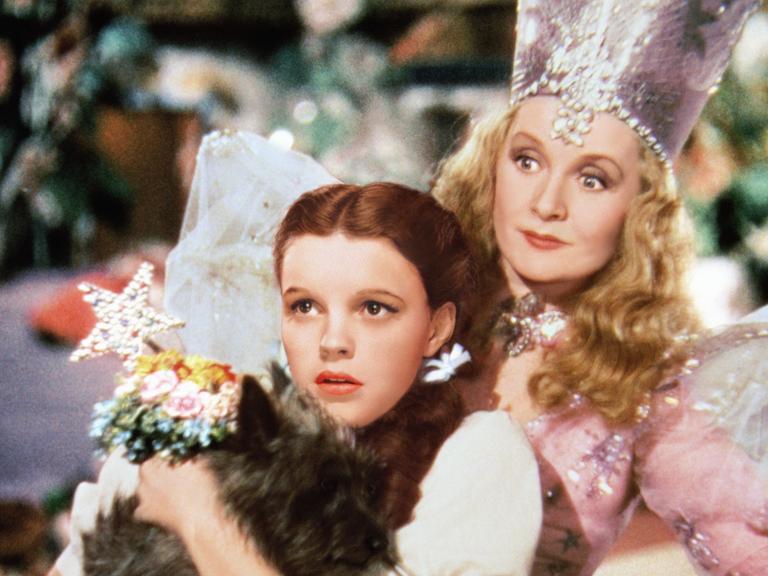 In dem Szenenbild von "Der Zauberer von Oz" schaut Judy Garland in der Rolle der "Dorothy" gebannt nach vorn, hinter ihr steht Billie Burke als 'Glinda'.