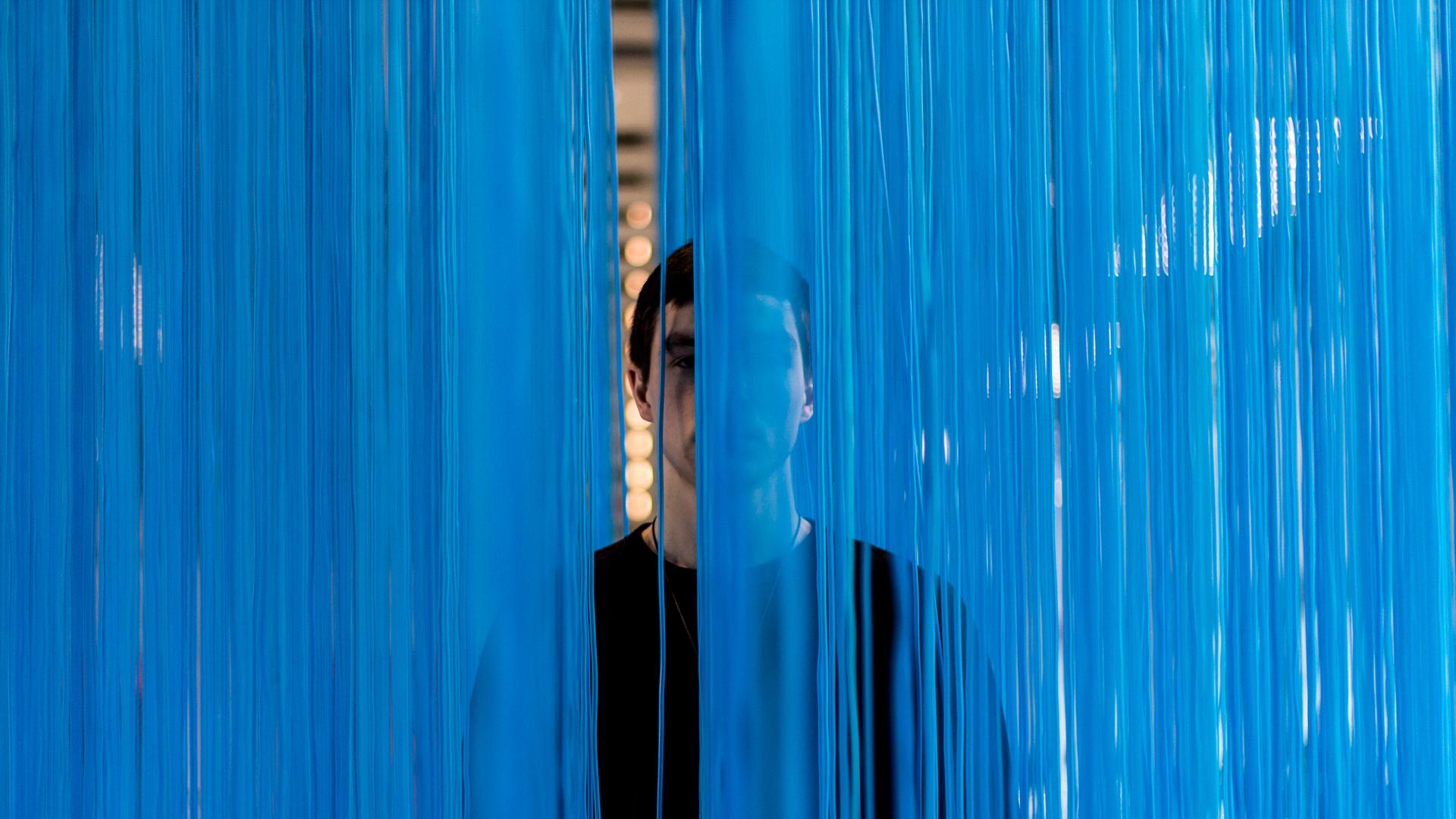 Eine Gestalt hinter blauem "Vorhang" von uneindeutiger Textur. In einem Spalt ist deutlich ein Ohr zu erkennen. Eine Gestalt hinter blauem "Vorhang" von uneindeutiger Textur. In einem Spalt ist deutlich ein Ohr zu erkennen.