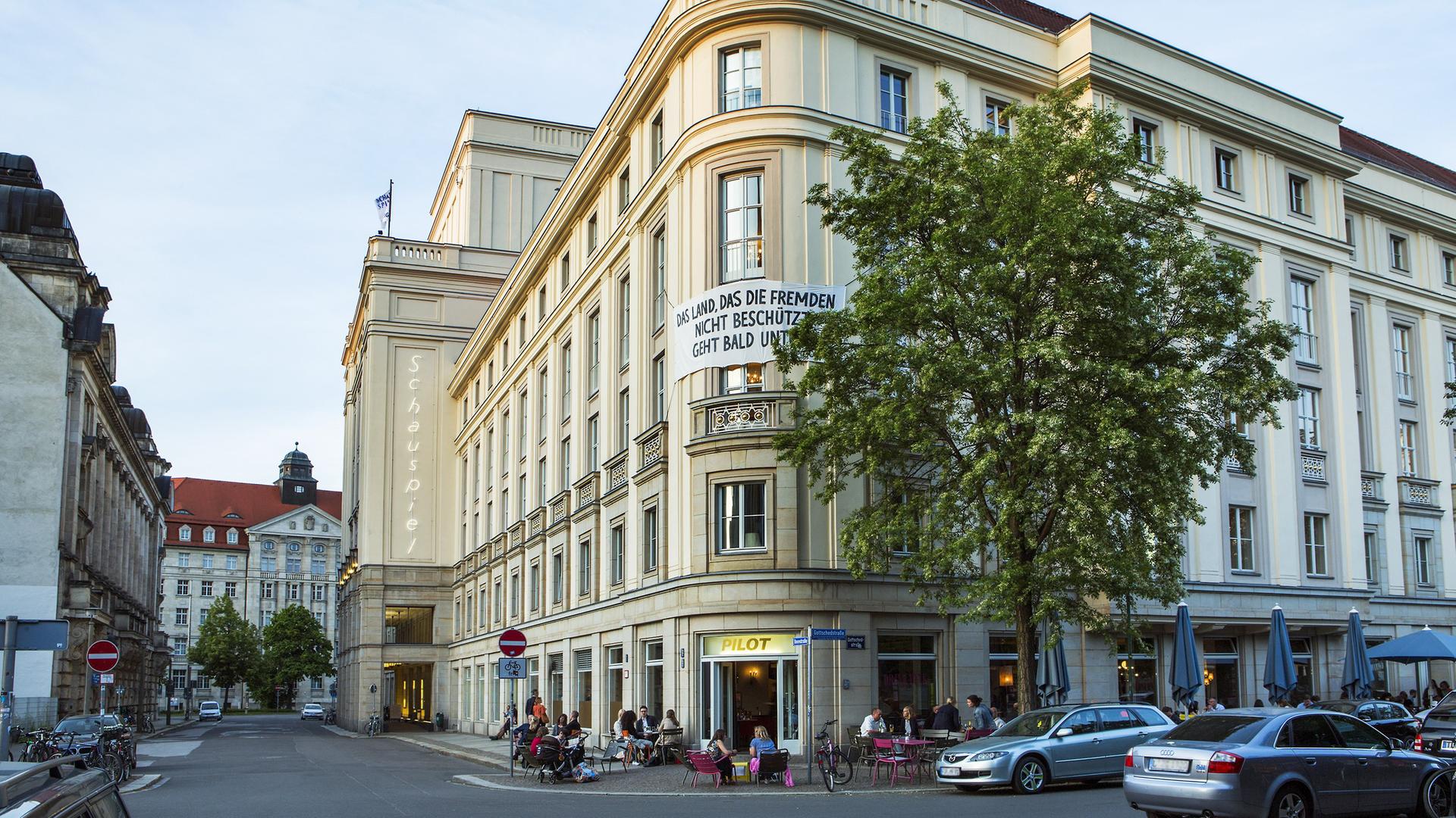Außenansicht des Schauspiel Leipzig. Ein Eckgebäude mit einem Transparent, auf dem steht: "Das Land, das die Fremden nicht beschützt, geht bald unter." Außenansicht des Schauspiel Leipzig. Ein Eckgebäude mit einem Transparent, auf dem steht: "Das Land, das die Fremden nicht beschützt, geht bald unter."