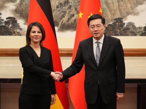 Baerbock und der chinesische Außenminister Qin Gang geben sich die Hand. Hinter ihnen die deutsche und die chinesische Flagge.