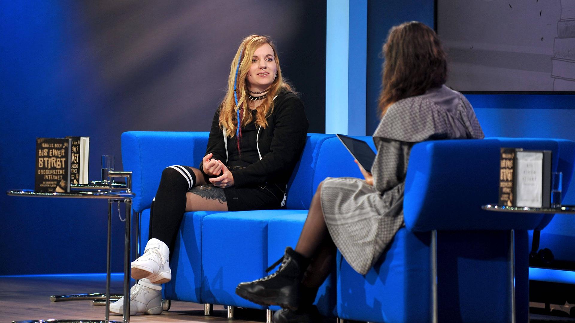 Die Journalistin Isabell Beer sitzt auf einem blauen Sofa auf der Frankfurter Buchmesse 2021 und wird von einer Moderatorin interviewt.