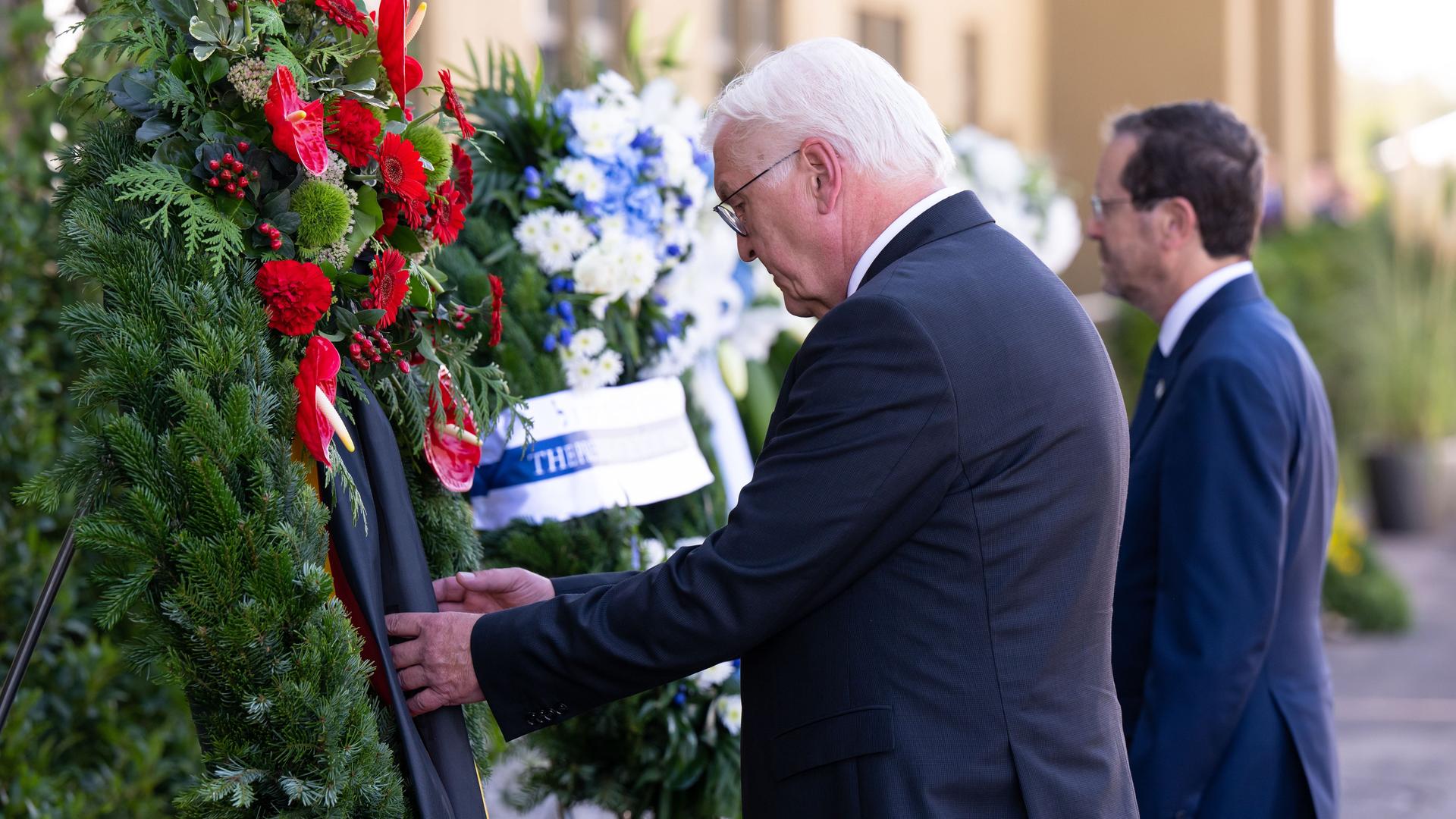 Bundes-Präsident Steinmeier und der israelische Staats-Chef Herzog stehen mit gesenktem kopf vor Blumen-Kränzen.