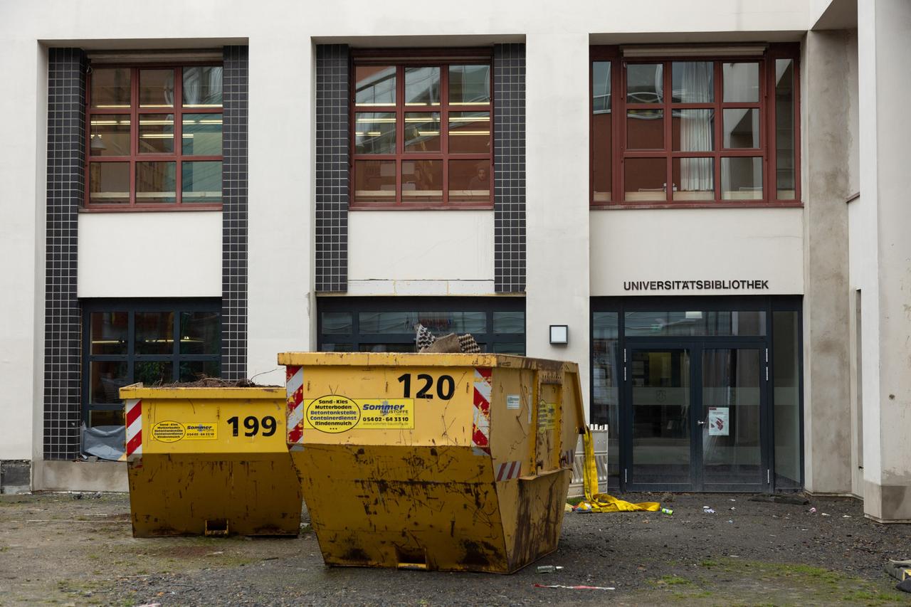 Bauabfall-Container stehen vor dem Eingang einer Universitätsbibliothek. Bauabfall-Container stehen vor dem Eingang einer Universitätsbibliothek.