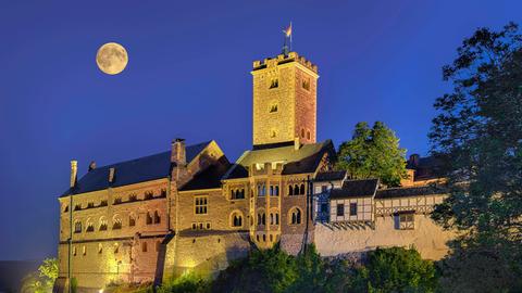 Die alten Mauern der Wartburg sind nachts erleuchtet, während ein Vollmond direkt über der Burg steht.