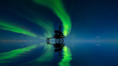 Eine Ölplattform in der Arktis, darüber Nordlichterscheinungen am Himmel.