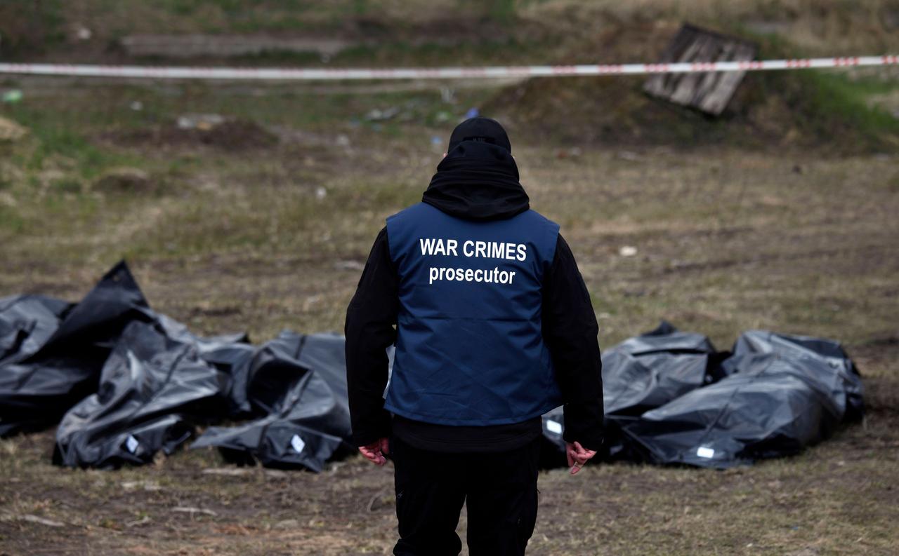 Eine Person steht vor mehreren Säcken, in denen sich Leichen befinden. Eine Person steht vor mehreren Säcken, in denen sich Leichen befinden.