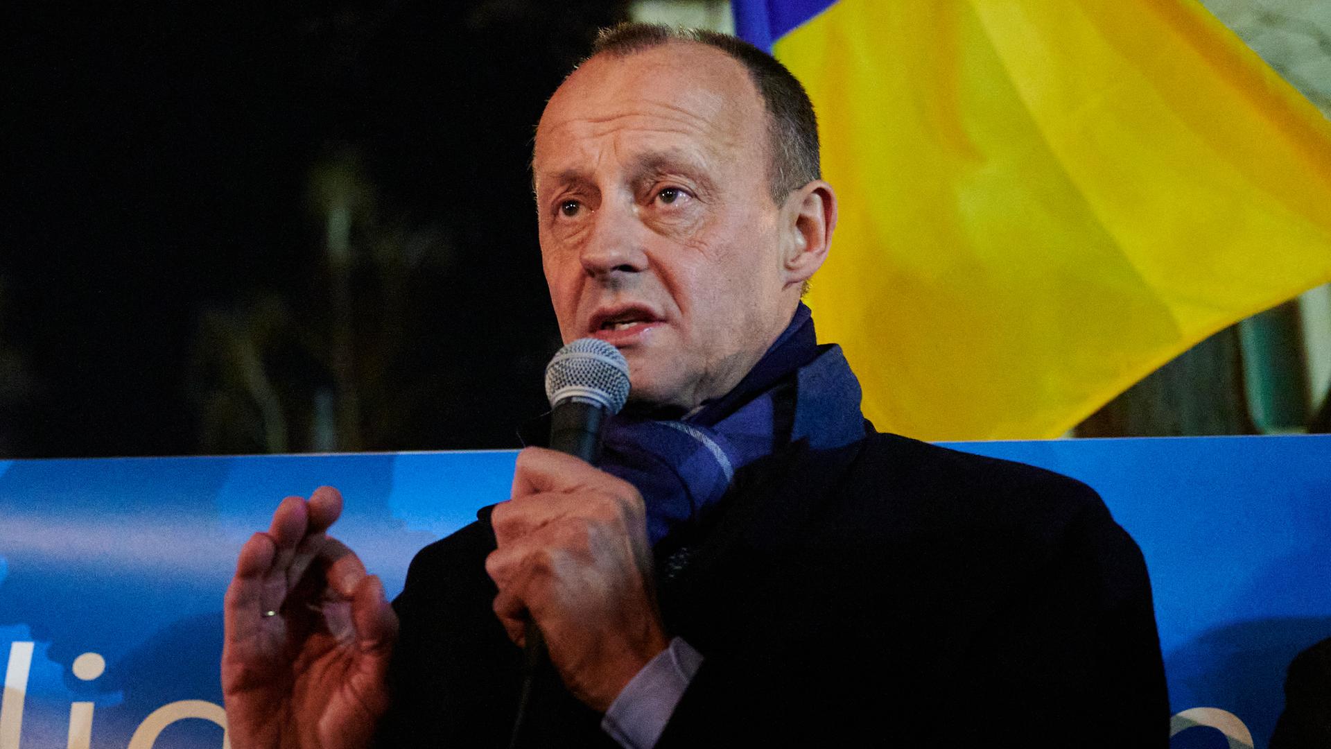 Friedrich Merz steht am späten Abend auf der Straße und spricht engagiert in ein Mikrofon, hinter ihm weht die gelb-blaue Flagge der Ukraine.