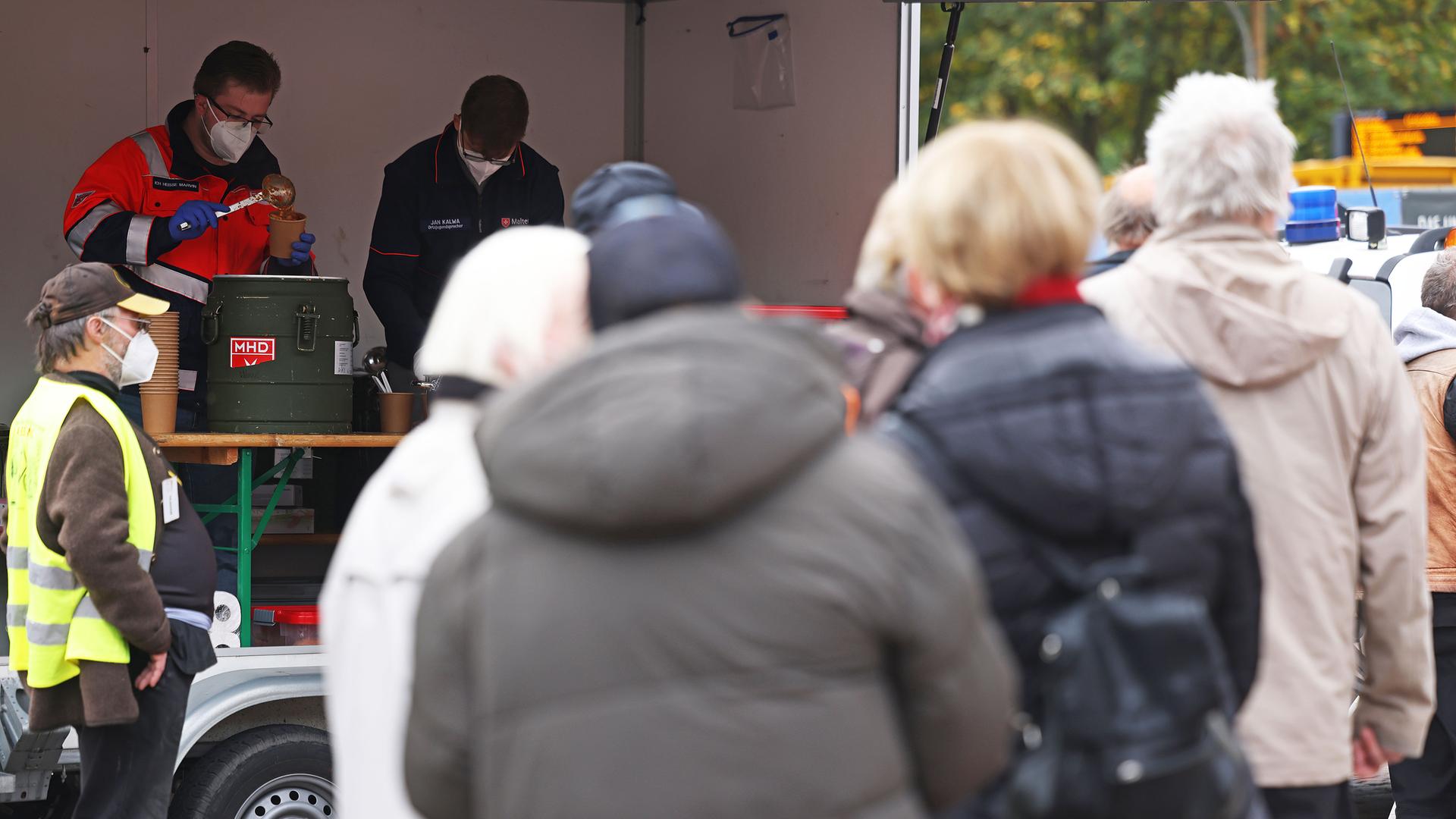 Menschen stehen vor einer Essensausgabe auf einem Platz an. Menschen stehen vor einer Essensausgabe auf einem Platz an.