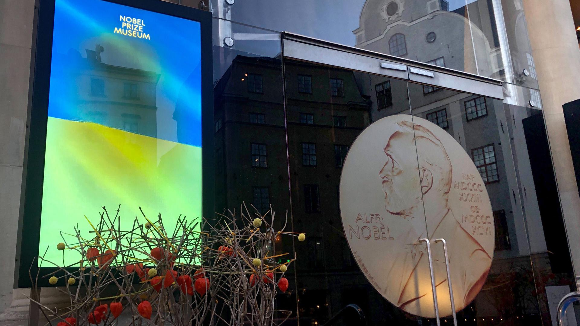 Auf einem Bildschirm vor dem Nobelpreismuseum in Stockholm ist eine Ukraine-Flagge zu sehen mit dem Schriftzug "May peace come to this piece of our beautiful world".