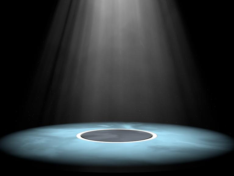Auf einer Theaterbühne wird ein Kreis in der Mitte mit einem Spotlight bestrahlt.