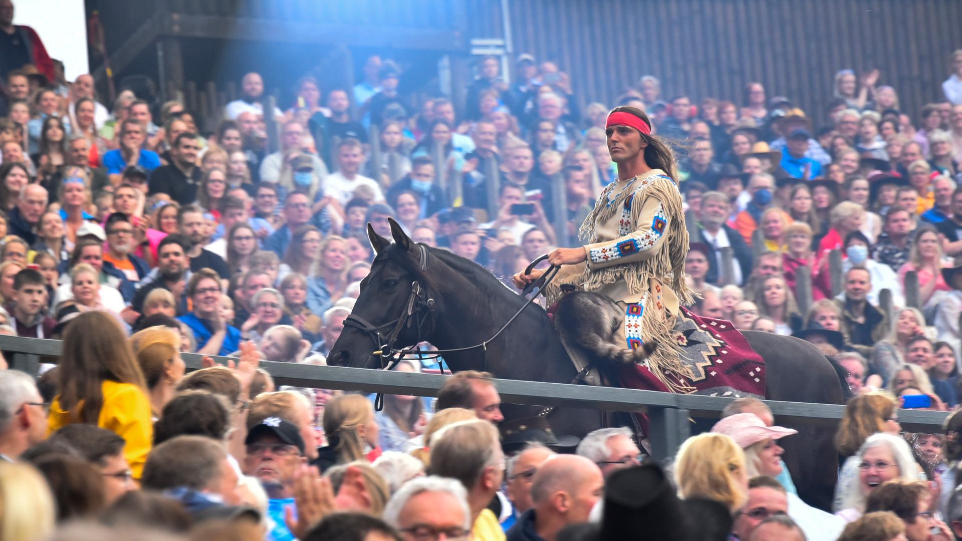 Ein Mann auf einen Pferd mit Federschmuck reitet durch eine Menschenmenge: Aufführung von "Der Ölprinz" bei den Karl May Spielen 2022 in Bad Segeberg.