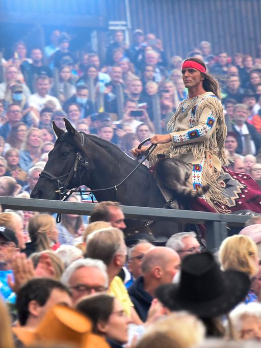 Ein Mann auf einen Pferd mit Federschmuck reitet durch eine Menschenmenge: Aufführung von "Der Ölprinz" bei den Karl May Spielen 2022 in Bad Segeberg.