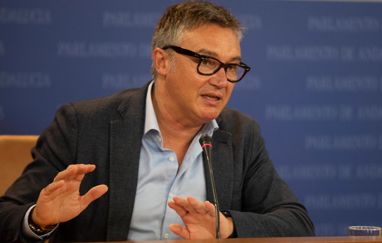 Ein Mann mit Brille und Jacket gestikuliert an einem Tisch sitzend. Ein Mann mit Brille und Jacket gestikuliert an einem Tisch sitzend.
