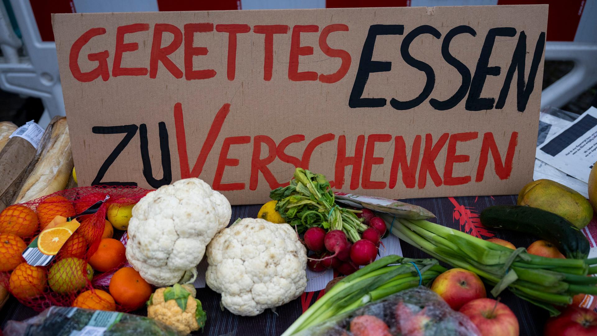 Ein Schild mit der Aufschrift "Gerettetes Essen zu verschenken" und zahlreiche Lebensmittel liegen auf einem Tisch am Stand der Klimaaktivisten von der Initiative "Aufstand der letzten Generation". 