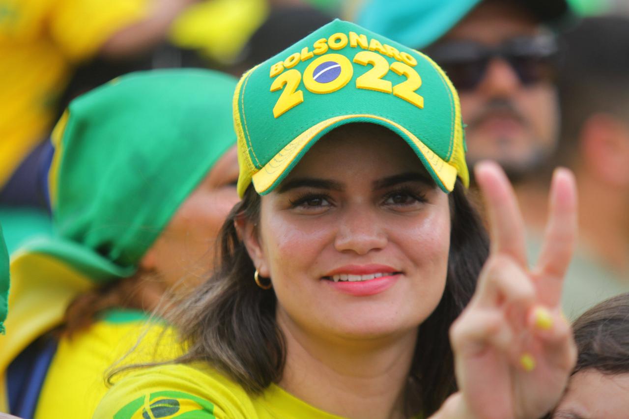 Eine junge Frau in gelbem Shirt trägt ein grünes Käppi auf dem "Bolsonaro 2022" steht.