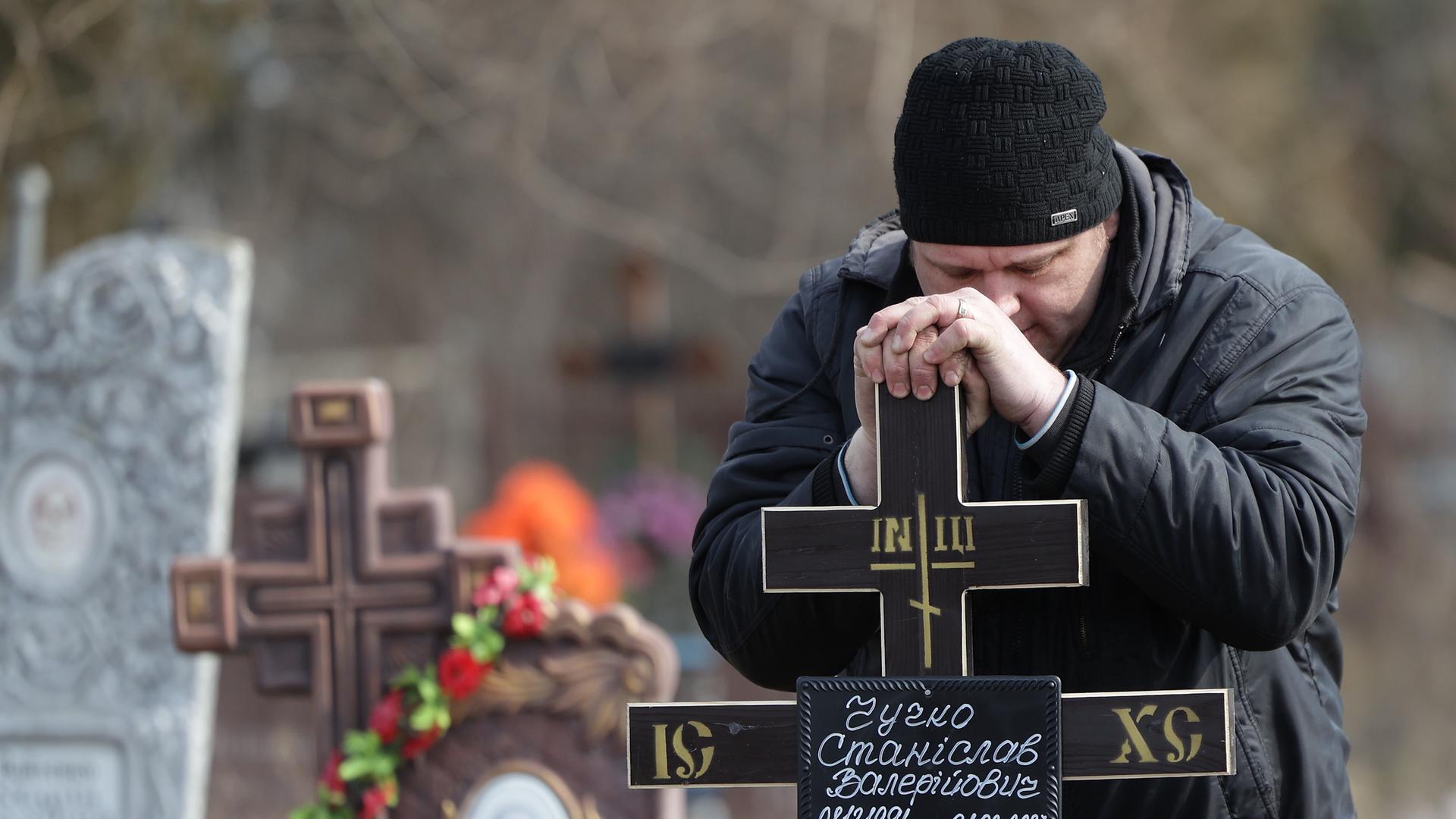 Ein Mann legt ein Kreuz auf das Grab eines ukrainischen Soldaten, der im Kampf um die Stadt Bachmut im Osten der Ukraine getötet wurde. Ein Mann legt ein Kreuz auf das Grab eines ukrainischen Soldaten, der im Kampf um die Stadt Bachmut im Osten der Ukraine getötet wurde.