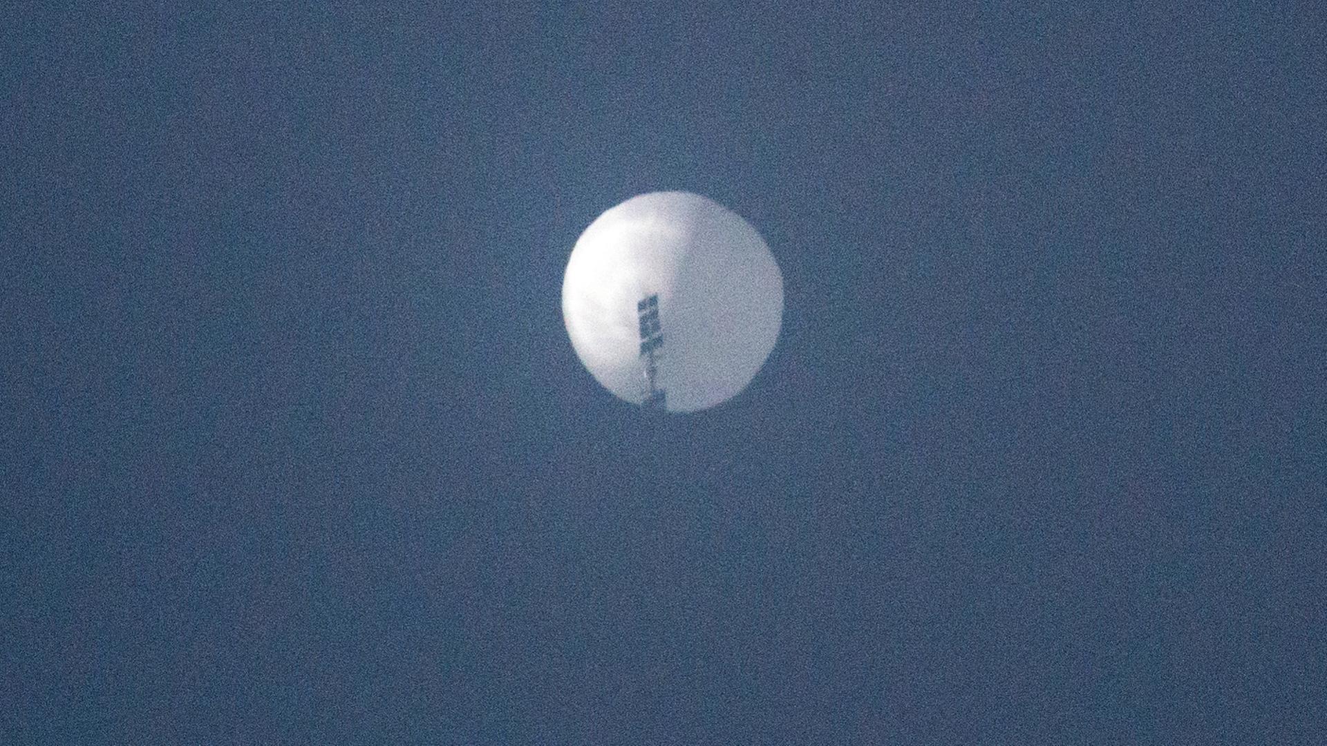 Man sieht den weißen Ballon weit entfernt von unten vor blauem Himmel.