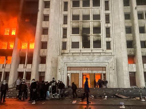 Protestierende stehen vor dem brennenden Rathaus von Almaty in Kasachstan. 