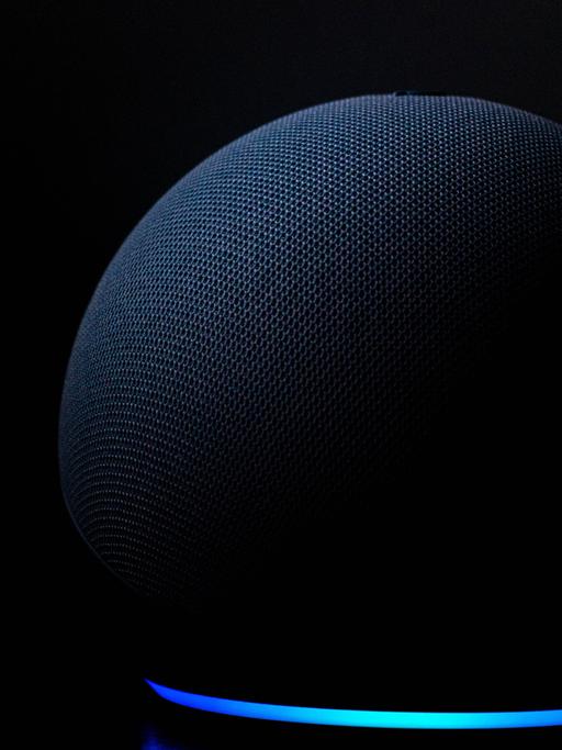 Nahaufnahme eines dunkelblauen Lautsprechers der Marke Echo Dot mit der Sprachassistenz Alexa von Amazon vor schwarzem Hintergrund. 