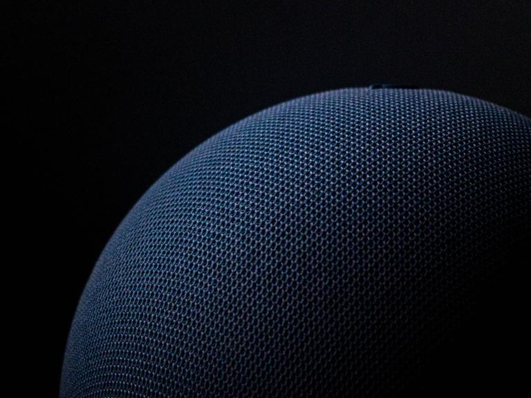 Nahaufnahme eines dunkelblauen Lautsprechers der Marke Echo Dot mit der Sprachassistenz Alexa von Amazon vor schwarzem Hintergrund. 