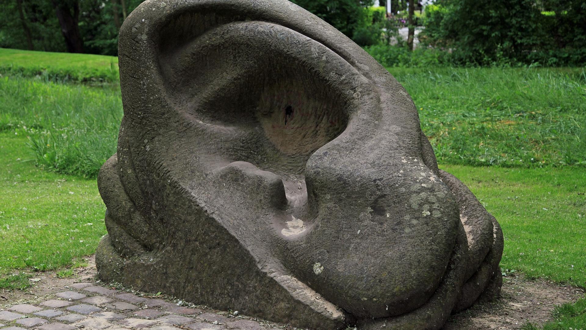 Eine Steinmetzarbeit zeigt ein Ohr, das auf einer Rasenfläche liegt. Eine Steinmetzarbeit zeigt ein Ohr, das auf einer Rasenfläche liegt.