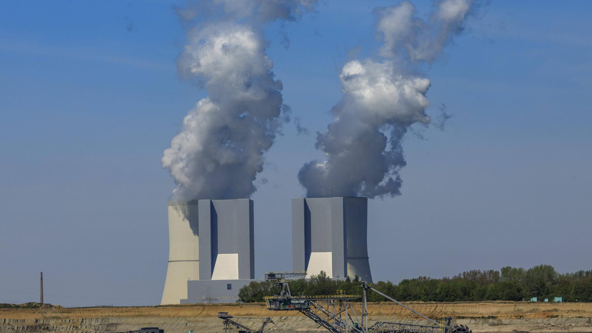 Im Vordergrund steht ein Bagger zum Abbau von Kohle. Weiter hinten sind rauchende Schlote und ein Kohlekraftwerk. Im Vordergrund steht ein Bagger zum Abbau von Kohle. Weiter hinten sind rauchende Schlote und ein Kohlekraftwerk.