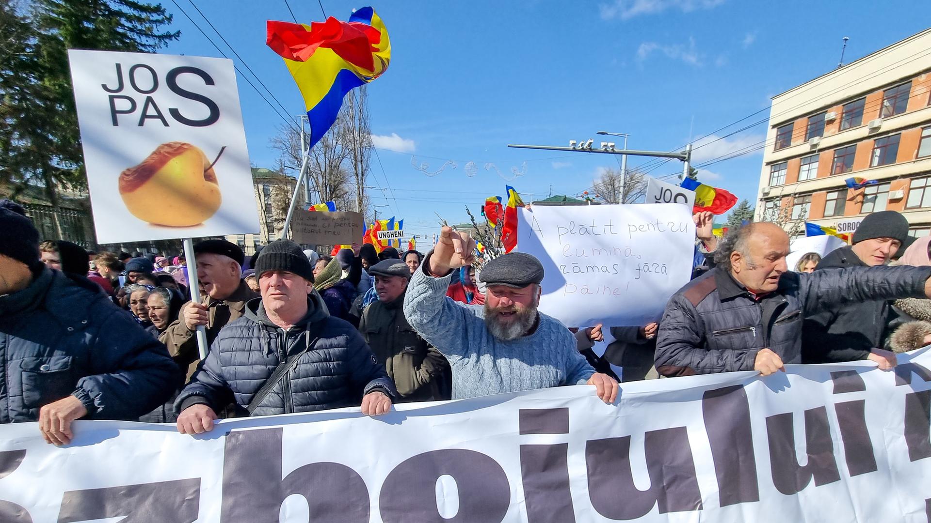 Demonstranten laufen über eine Straße. Sie halten ein Banner und schwenken die moldawische Fahne.