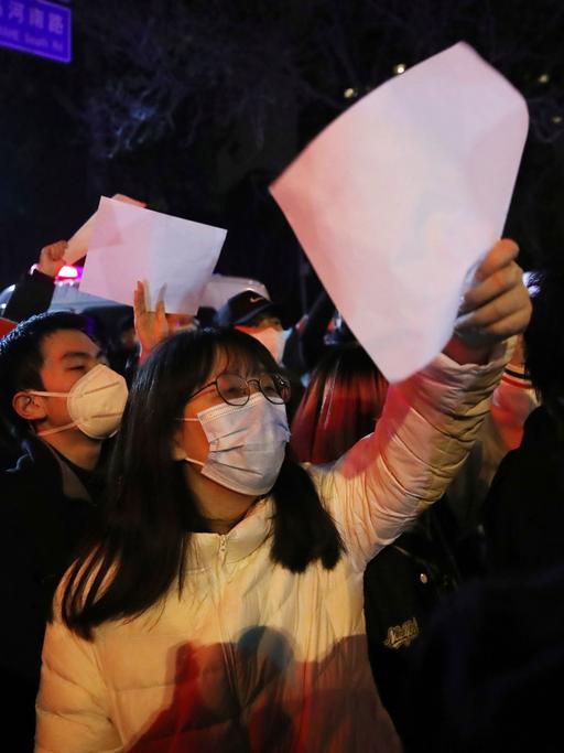 Mehrere Menschen demonstrieren gegen Chinas Null-Covid-Politik in Peking und halten weiße, unbeschriftete Zettel in die Höhe.