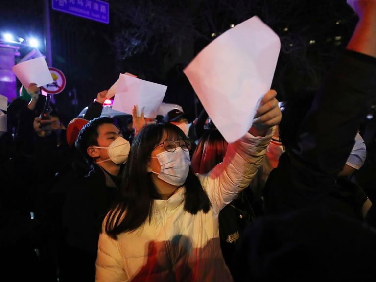 Mehrere Menschen demonstrieren gegen Chinas Null-Covid-Politik in Peking und halten weiße, unbeschriftete Zettel in die Höhe.