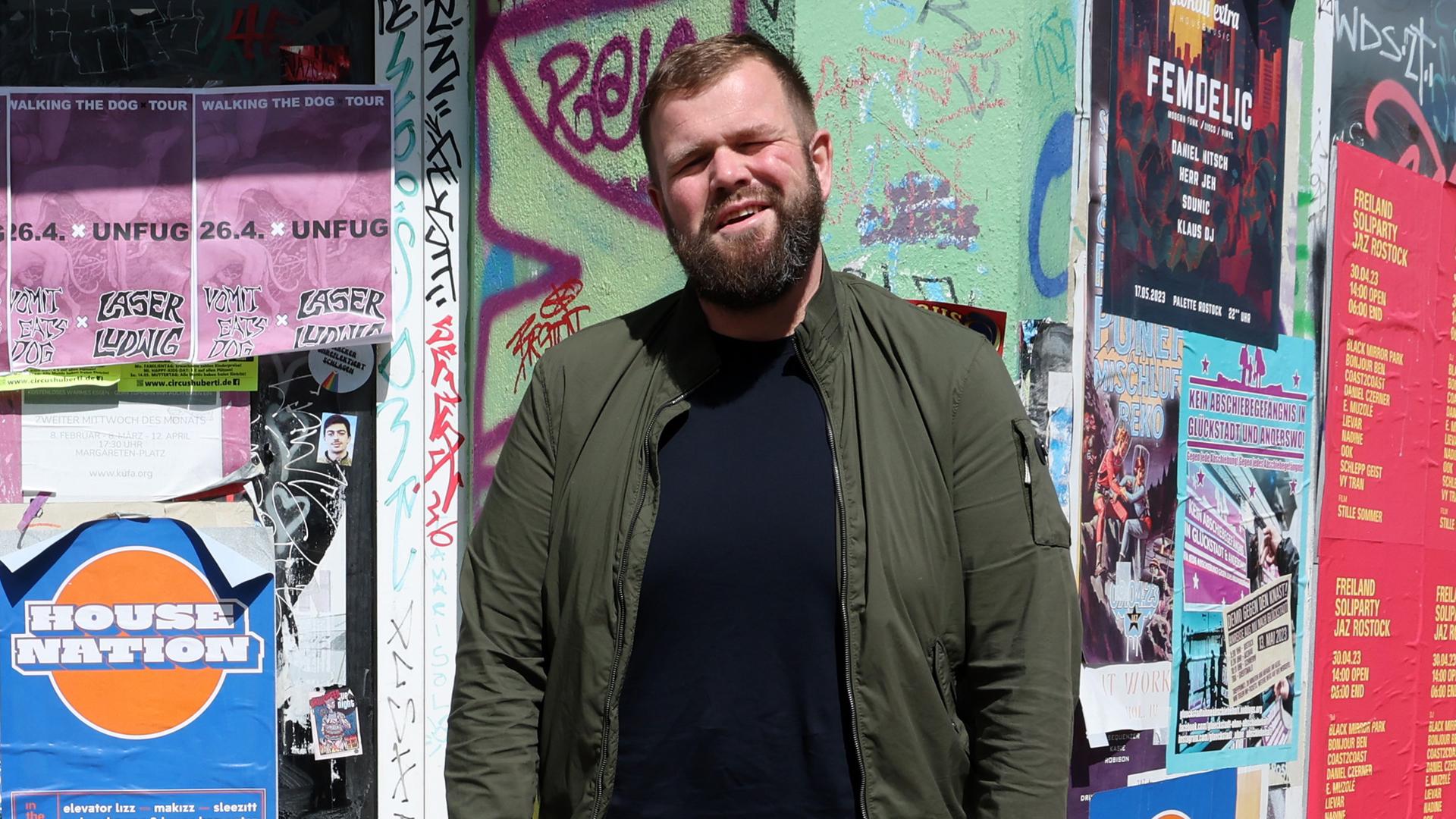 Jan "Monchi" Gorkow, Sänger und Frontmann der Band Feine Sahne Fischfilet, steht vor eine Tür eines Hauses. An dem Haus sind viele Plakate geklebt. Jan "Monchi" Gorkow, Sänger und Frontmann der Band Feine Sahne Fischfilet, steht vor eine Tür eines Hauses. An dem Haus sind viele Plakate geklebt.