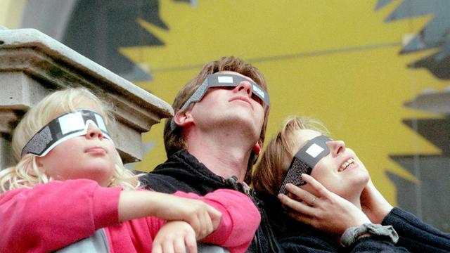 Eine Familie betrachtet am 11.8.1999 vor dem Hintergrund einer überdimensionalen stilisierten Sonne die Sonnenfinsternis