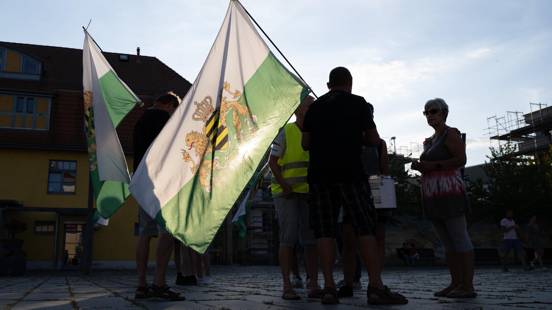 Teilnehmer einer Kundgebung der rechtsextremen Kleinstpartei "Freie Sachsen" stehen mit einer Fahne des einstigen Königreiches Sachsen auf einem Markplatz Teilnehmer einer Kundgebung der rechtsextremen Kleinstpartei "Freie Sachsen" stehen mit einer Fahne des einstigen Königreiches Sachsen auf einem Markplatz