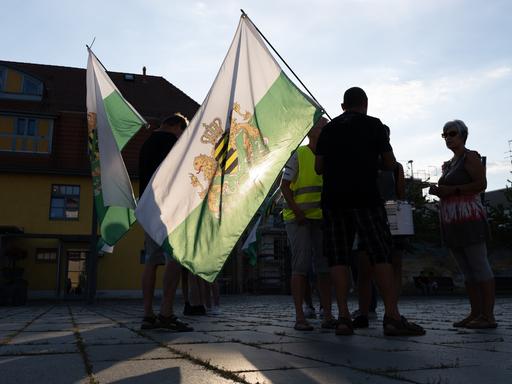 Teilnehmer einer Kundgebung der rechtsextremen Kleinstpartei "Freie Sachsen" stehen mit einer Fahne des einstigen Königreiches Sachsen auf einem Markplatz