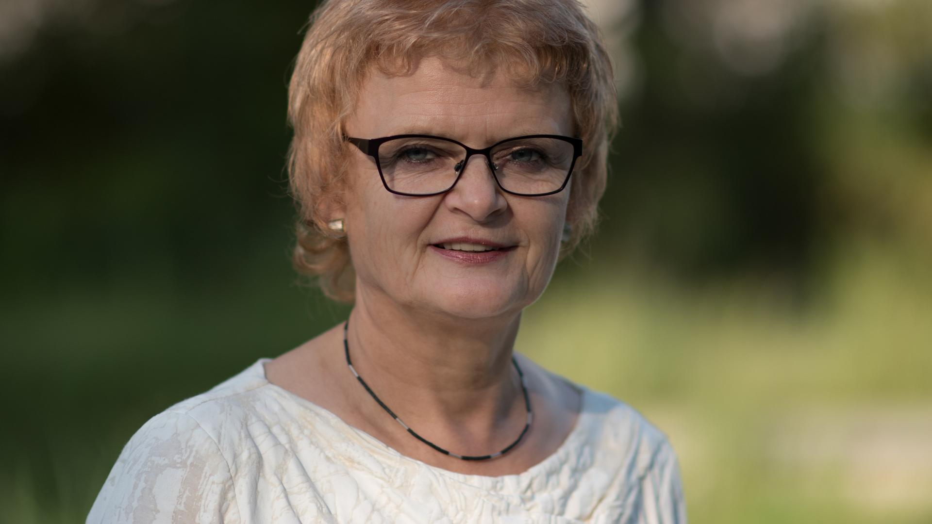 Die Soziologin Maria Nooke steht in der Landschaft, trägt eine schwarze Brille und lächelt in die Kamera.