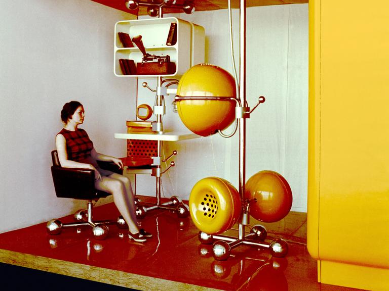 Eine Frau sitzt auf einem Stuhl. Sie blickt auf einen futuristischen halbkugelförmigen Bildschirm.
