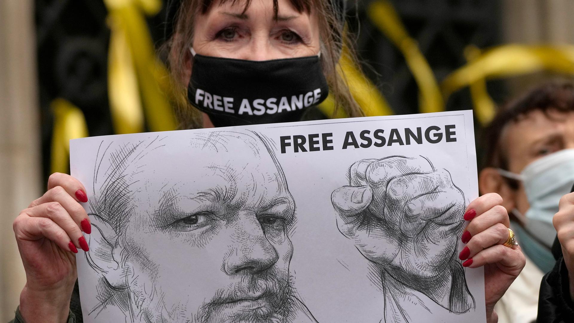 Eine Frau trägt einen Mundschutz mit der Aufschrift Free Assange, in den Händen ein Porträt Assanges Eine Frau trägt einen Mundschutz mit der Aufschrift Free Assange, in den Händen ein Porträt Assanges
