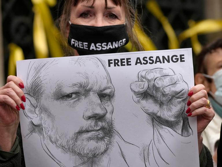 Eine Frau trägt einen Mundschutz mit der Aufschrift Free Assange, in den Händen ein Porträt Assanges
