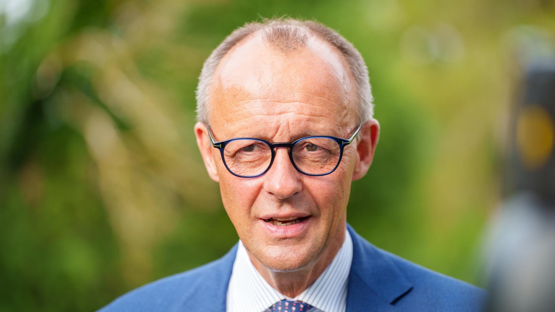 Friedrich Merz trägt ein blaues Sacko, ein weißblau gestreiftes Hemd. Er spricht und schaut an der Kamera vorbei. Friedrich Merz trägt ein blaues Sacko, ein weißblau gestreiftes Hemd. Er spricht und schaut an der Kamera vorbei.