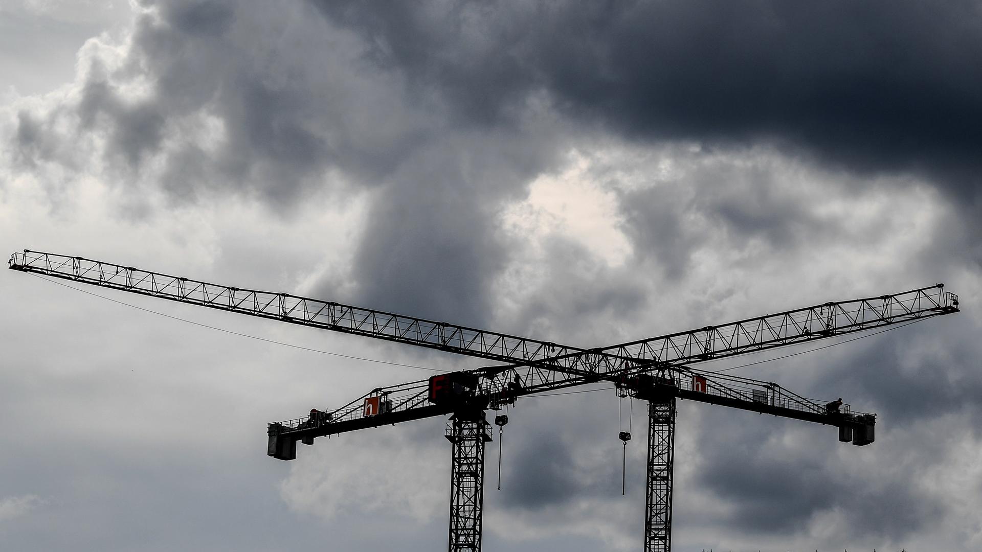 Baukräne sind vor dunklen Wolken zu sehen. Baukräne sind vor dunklen Wolken zu sehen.