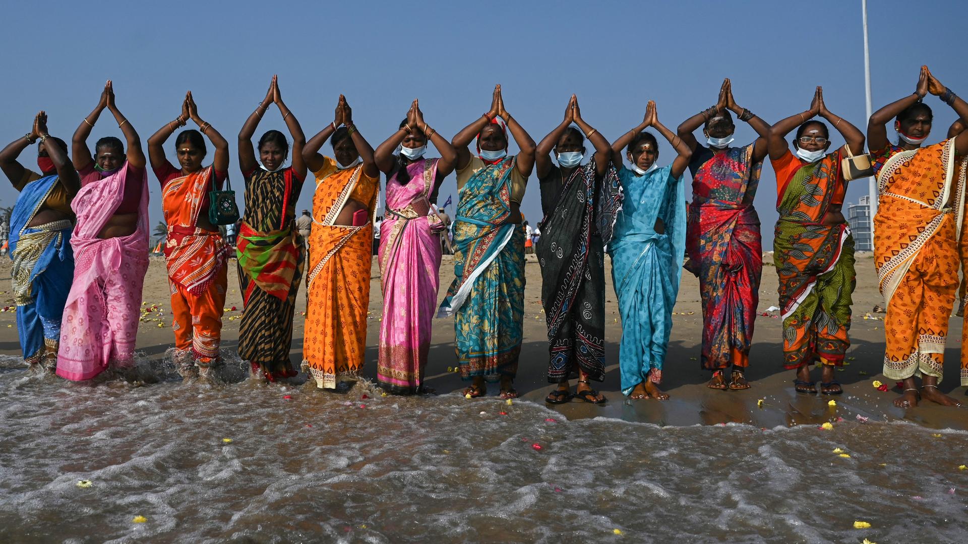 Frauen stehen aufgereiht nebeneinander am Strand im Wasser, ihre Arme führen sie über dem Kopf zusammen.