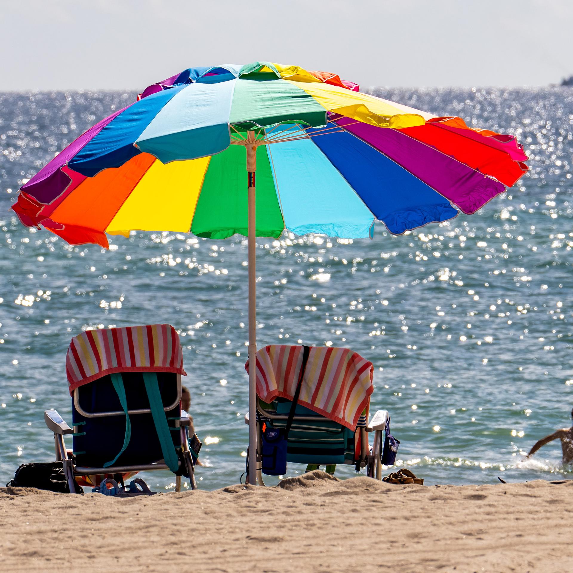 Ein bunter Sonnenschirm am Strand, im Meer planschen ein Kind und eine Frau