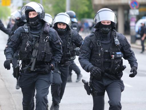 Polizisten mit Helmen und Schutzkleidung laufen eine Straße entlang.