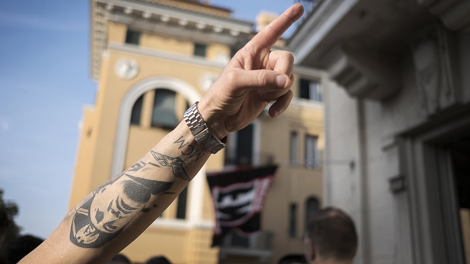 Aufnahme eines Armes mit erhobenem Zeigefinger und einem Tattoo mit dem Gesicht von Benito Mussolini. Aufnahme eines Armes mit erhobenem Zeigefinger und einem Tattoo mit dem Gesicht von Benito Mussolini.