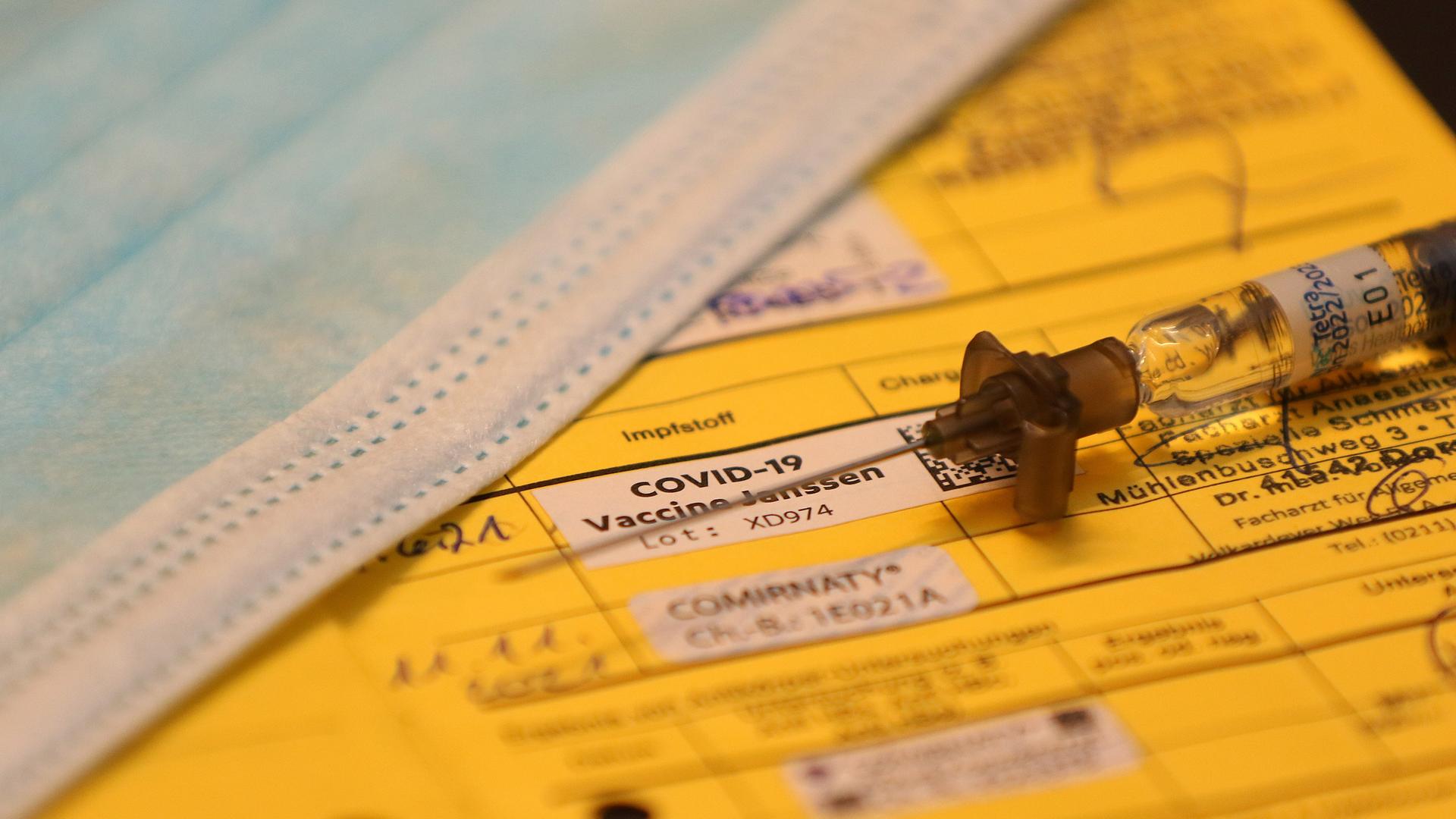 Symbolfoto zum Thema Impfung und Impfpass. Eine Spritze liegt auf einem aufgeschlagenen Impfpass. Auch der Teil einer Mund-Nasen-Maske ist zu sehen. Symbolfoto zum Thema Impfung und Impfpass. Eine Spritze liegt auf einem aufgeschlagenen Impfpass. Auch der Teil einer Mund-Nasen-Maske ist zu sehen.