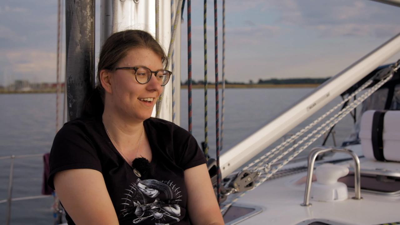 Eine junge Frau mit Brille und schwarzem T-Shirt sitzt an Bord einer Segeljacht.
