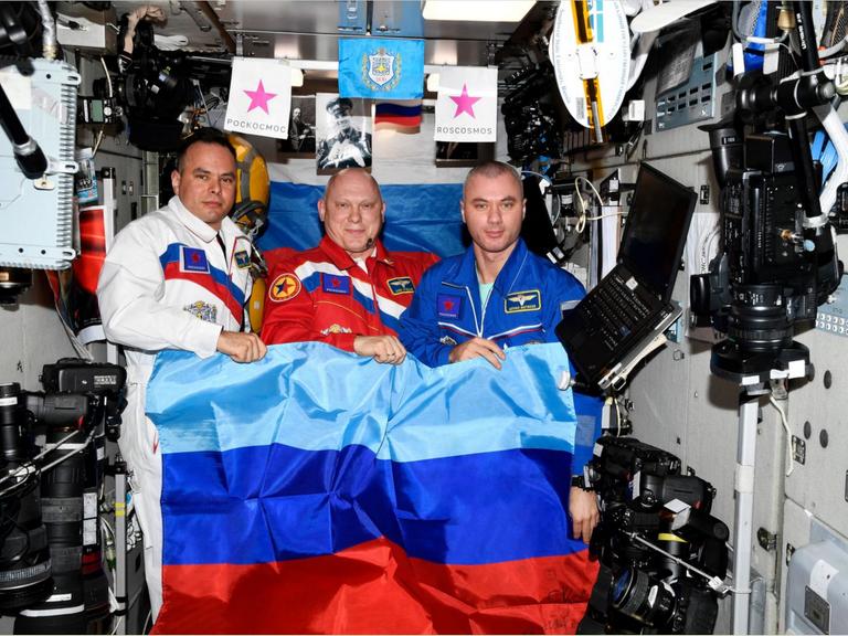 Das Ende aller ISS-Illusionen: Drei Kosmonauten – gekleidet in die russischen Nationalfarben – posieren auf der Raumstation mit der Flagge der besetzten „Volksrepublik“ Luhansk.