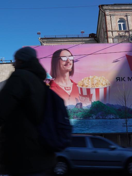 Auf einem Foto vom 4. Februar 2022 ist ein Passant zu sehen, der an einem großen Werbeplakat für ein Multiplex-Kino vorbeiläuft. Auf dem Plakat ist ein Mann mit Popcorn zu sehen.