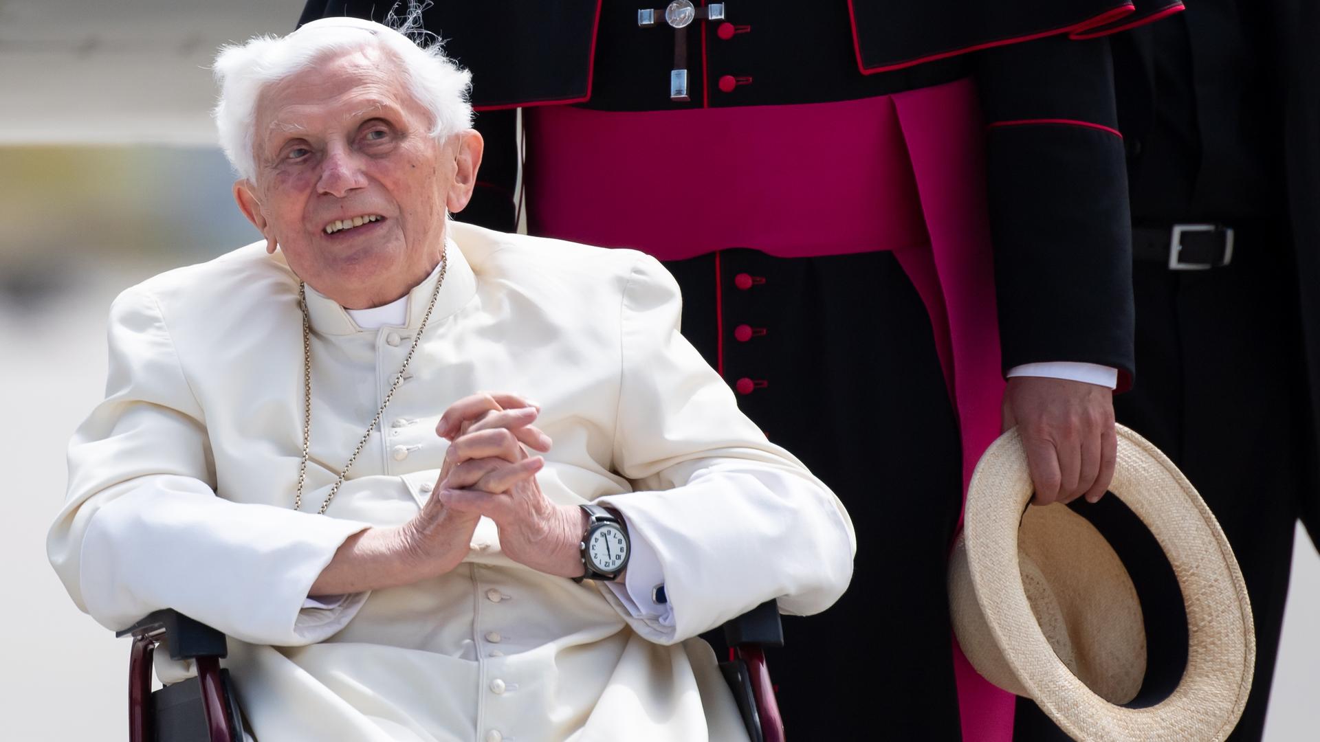 Der frühere Papst Benedikt der Sechzehnte sitzt in einem Stuhl und hat die Hände gefaltet.