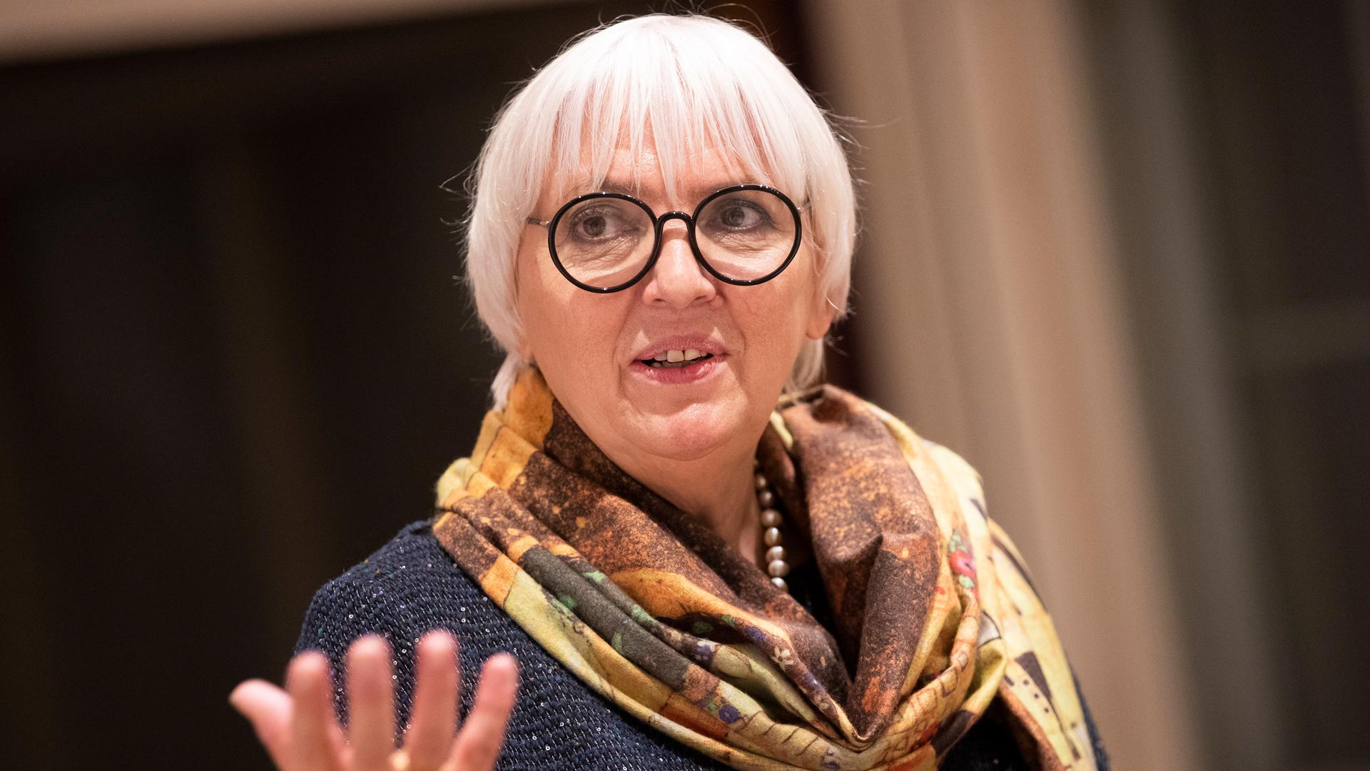 Claudia Roth, mit schwarz gerahmter Brille und einem sandfarbenen Seidentuch um den Hals, gestikuliert bei einem Pressetermin. Claudia Roth, mit schwarz gerahmter Brille und einem sandfarbenen Seidentuch um den Hals, gestikuliert bei einem Pressetermin.