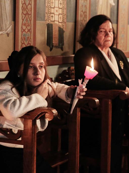 Eine junge Frau und eine alte Frau halten Kerzen in der Hand bei einer Feier der Auferstehung Jesu in einer Kirche in Albanien, 2023.